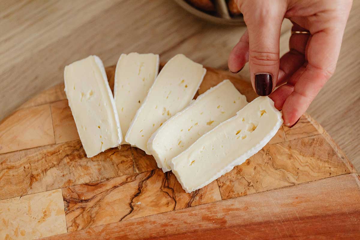 Un camembert de Normandie traditionnel présenté sur une planche en bois, accompagné de quelques tranches de pain rustique.