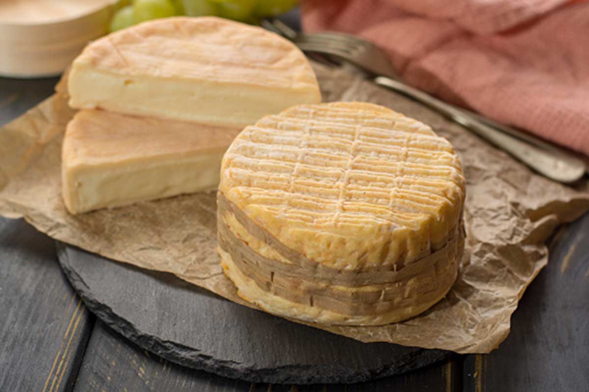 Un fromage Livarot traditionnel présenté sur une planche en bois, accompagné de pain frais et de figues.