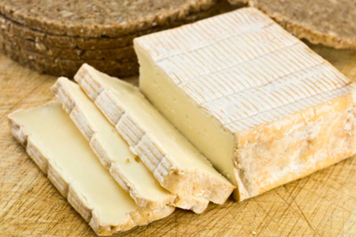 Un fromage Pont-l'Évêque traditionnel présenté sur une planche en bois, entouré de fruits frais et de noix.